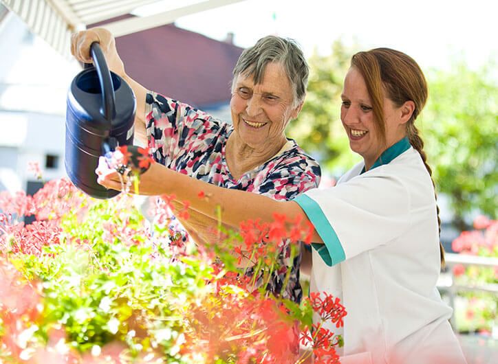 Pflegerin und Bewohnerin gießen gemeinsam Blumen