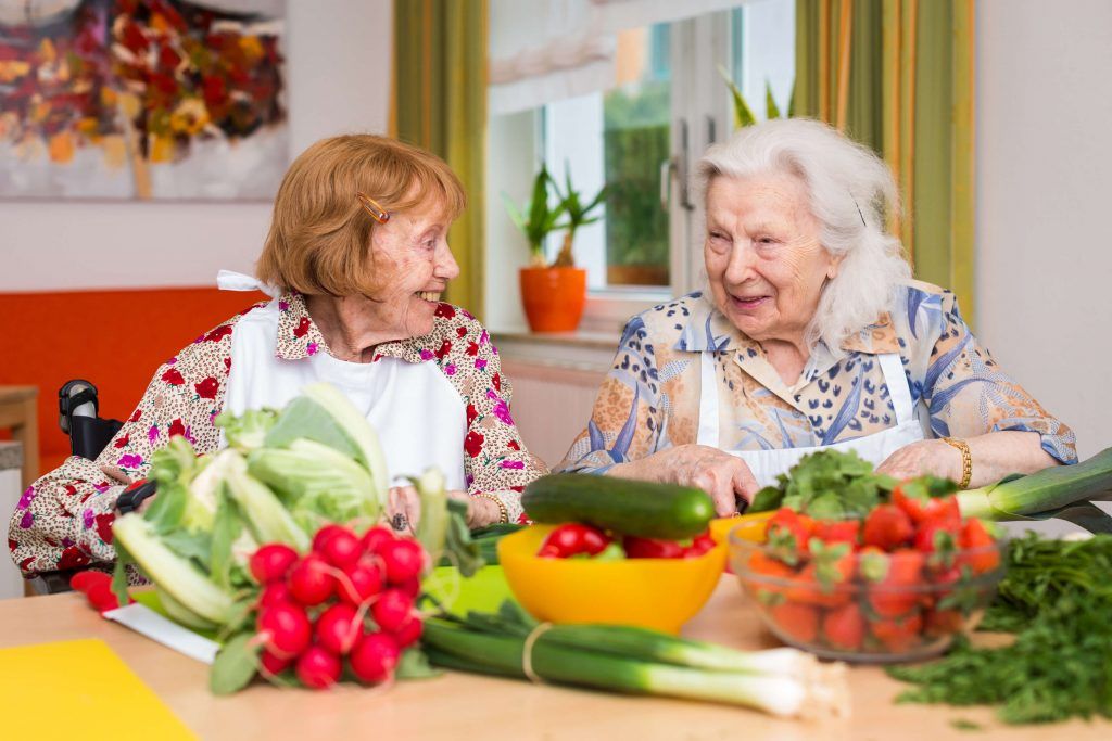 Zwei Bewohnerinnen sitzen am Tisch und schneiden Gemüse