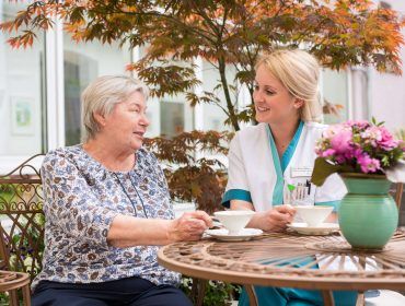 Bewohnerin und Pflegerin sitzen im Garten und trinken Kaffee