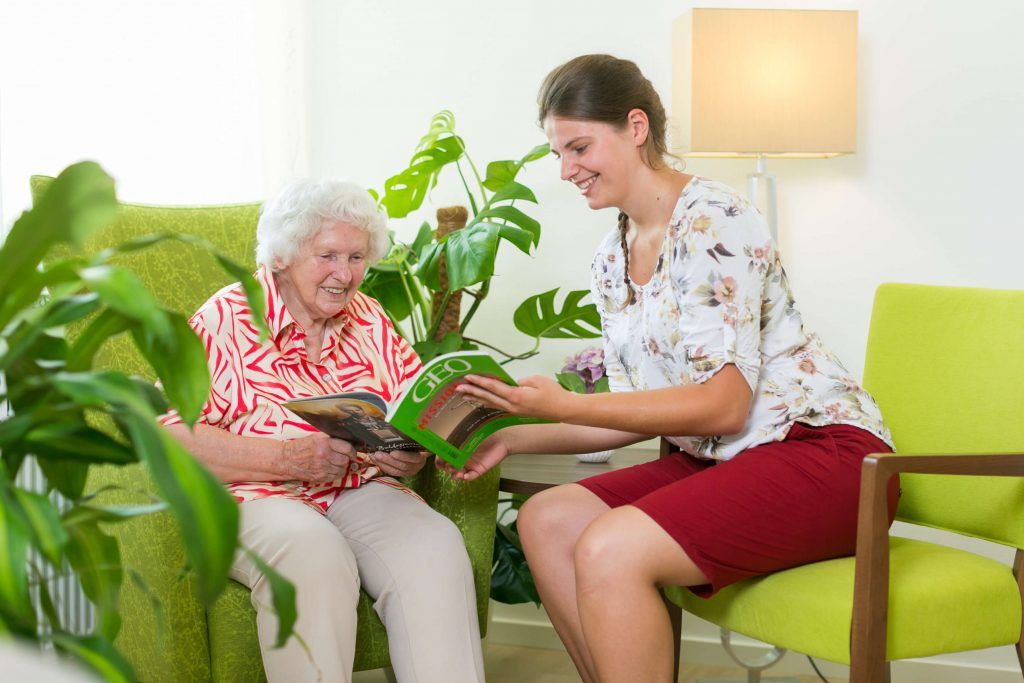 Ehrenamtliche Mitarbeiterin liest mit Bewohnerin gemeinsam eine Zeitschrift