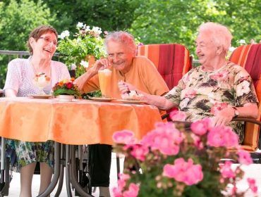Drei Bewohnerinnen sitzen mit Eiskaffee am Tisch und lachen