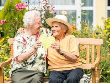 Zwei Bewohnerinnen sitzen auf Gartenbank und halten gemeinsam ein Herz aus Pappe