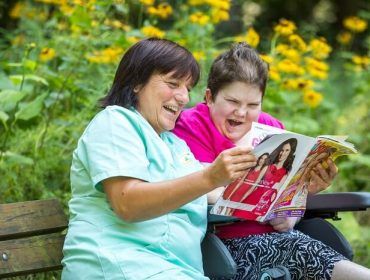 Pflegerin liest einer Bewohnerin eine Zeitschrift vor