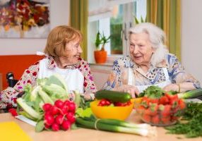 Zwei Bewohnerinnen sitzen am Tisch und schneiden Gemüse